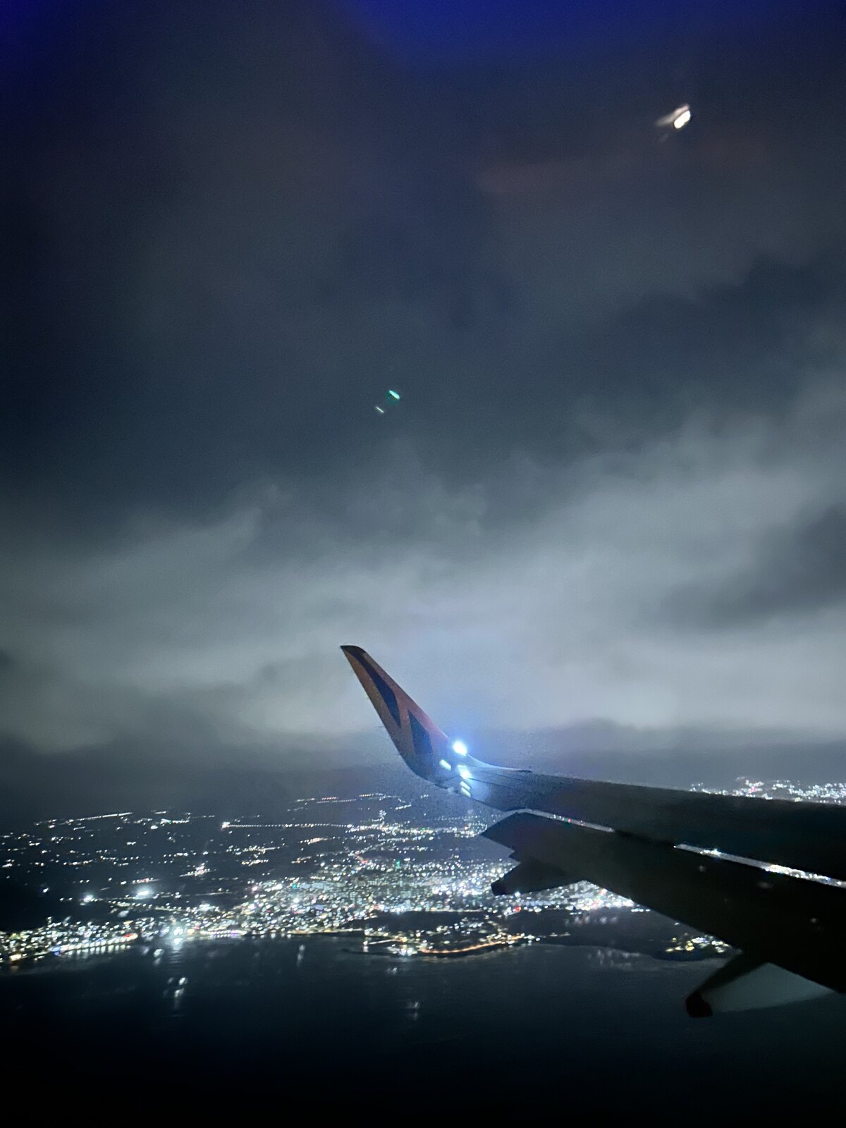 The view from a plane window at night, city lights below the wing