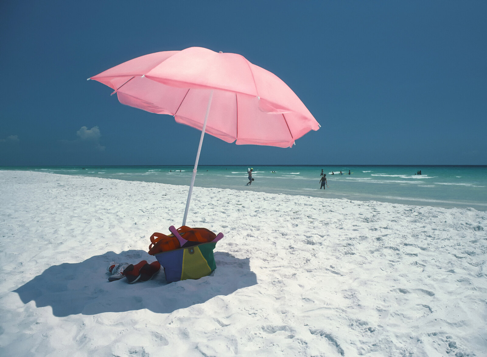 A pink parasol on the white quartz sand at Seaside, the Gulf emerald green behind it